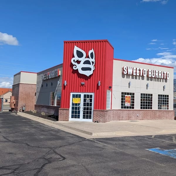Exterior of Sweeto Burrito restaurant with red and tan walls, a large logo, and parking lot.