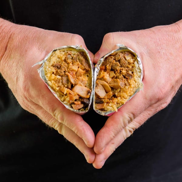 Hands forming a heart shape around two halves of a delicious Sweeto Burrito, revealing its savory filling.