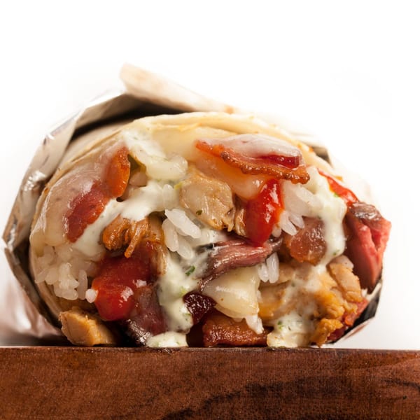 A Sweeto Burrito with meat, rice, and sauce, partially unwrapped from foil on a wooden surface.