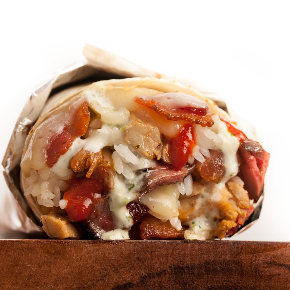 A Sweeto Burrito with meat, rice, and sauce, partially unwrapped from foil on a wooden surface.