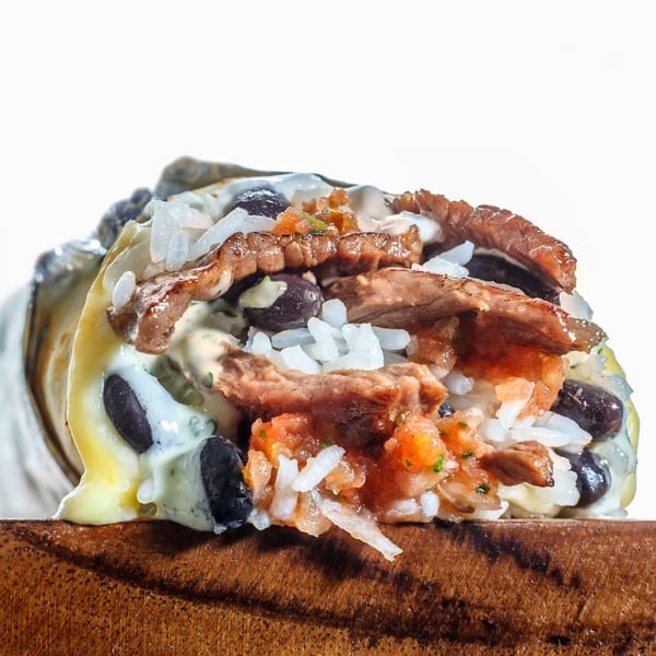 Close-up of a Sweeto Burrito with steak, rice, black beans, salsa, and creamy sauce.