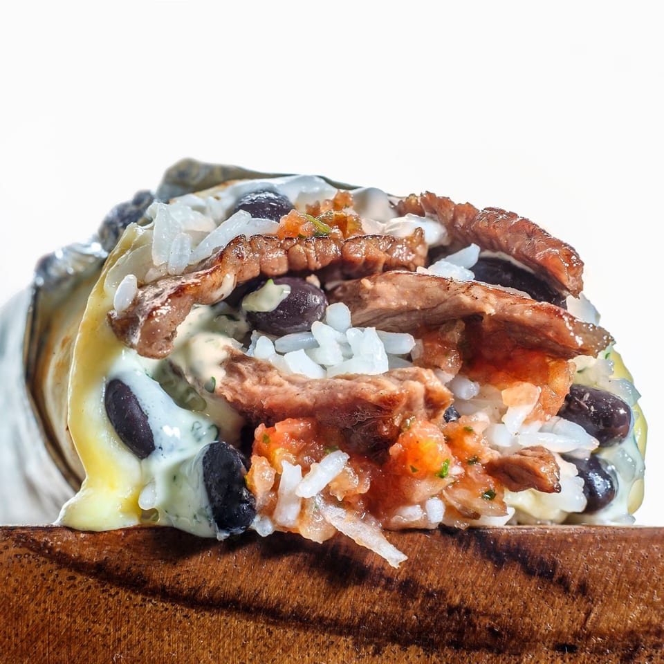 Close-up of a Sweeto Burrito with steak, rice, black beans, salsa, and creamy sauce.