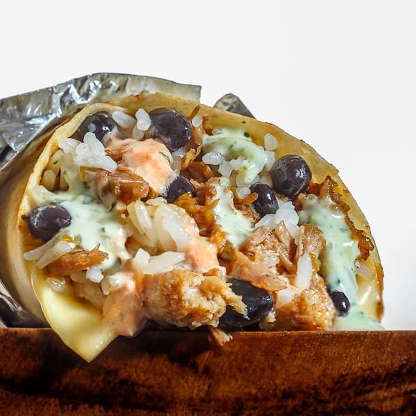 A close-up of a Sweeto Burrito, cut open to show rice, black beans, meat, and sauces.