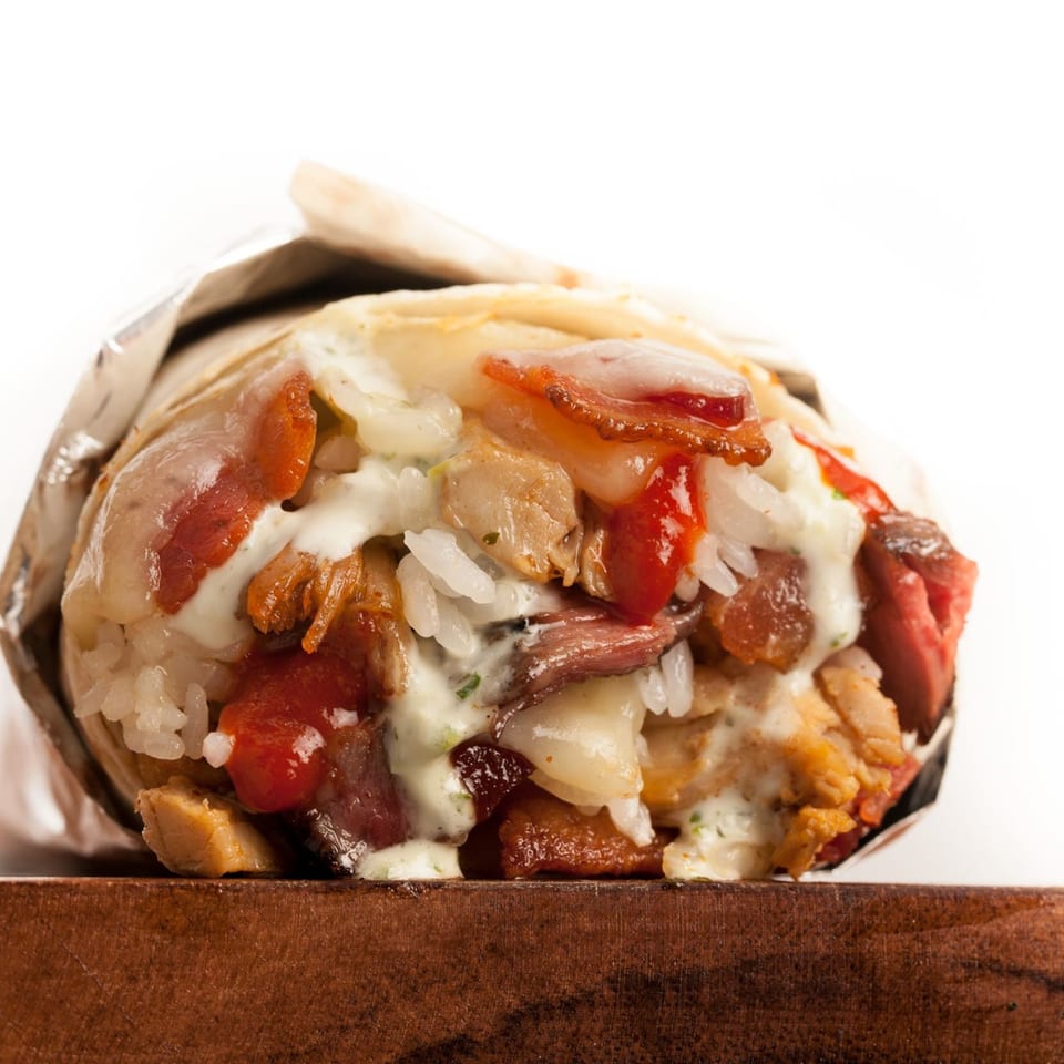 A large, open Sweeto Burrito with visible fillings of meat, rice, and sauces, wrapped in foil.