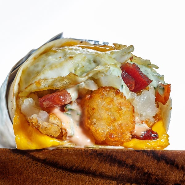 Close-up of a Sweeto Burrito with fried egg, bacon, tater tots, cheese, and sauce.